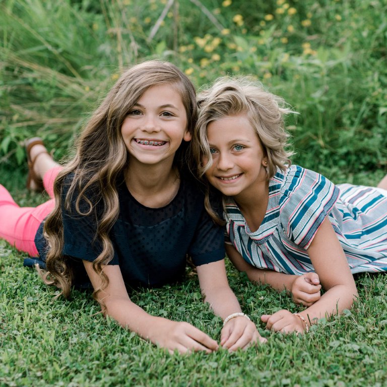 2 girls laying on the grass facing the camera smiling
