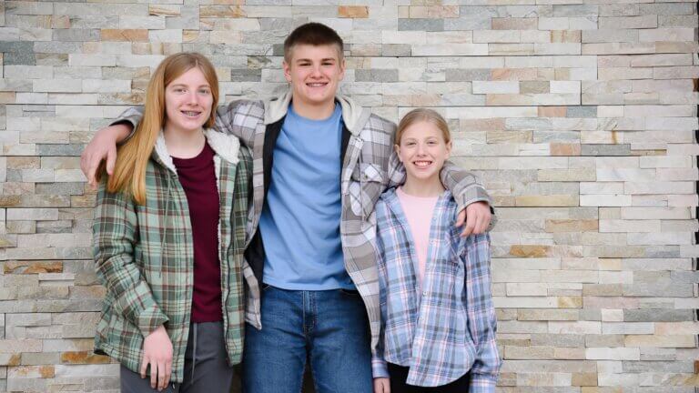 three siblings standing together in front of brick wall